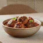 Homemade meatballs in tomato sauce in a rustic bowl on a wooden table.